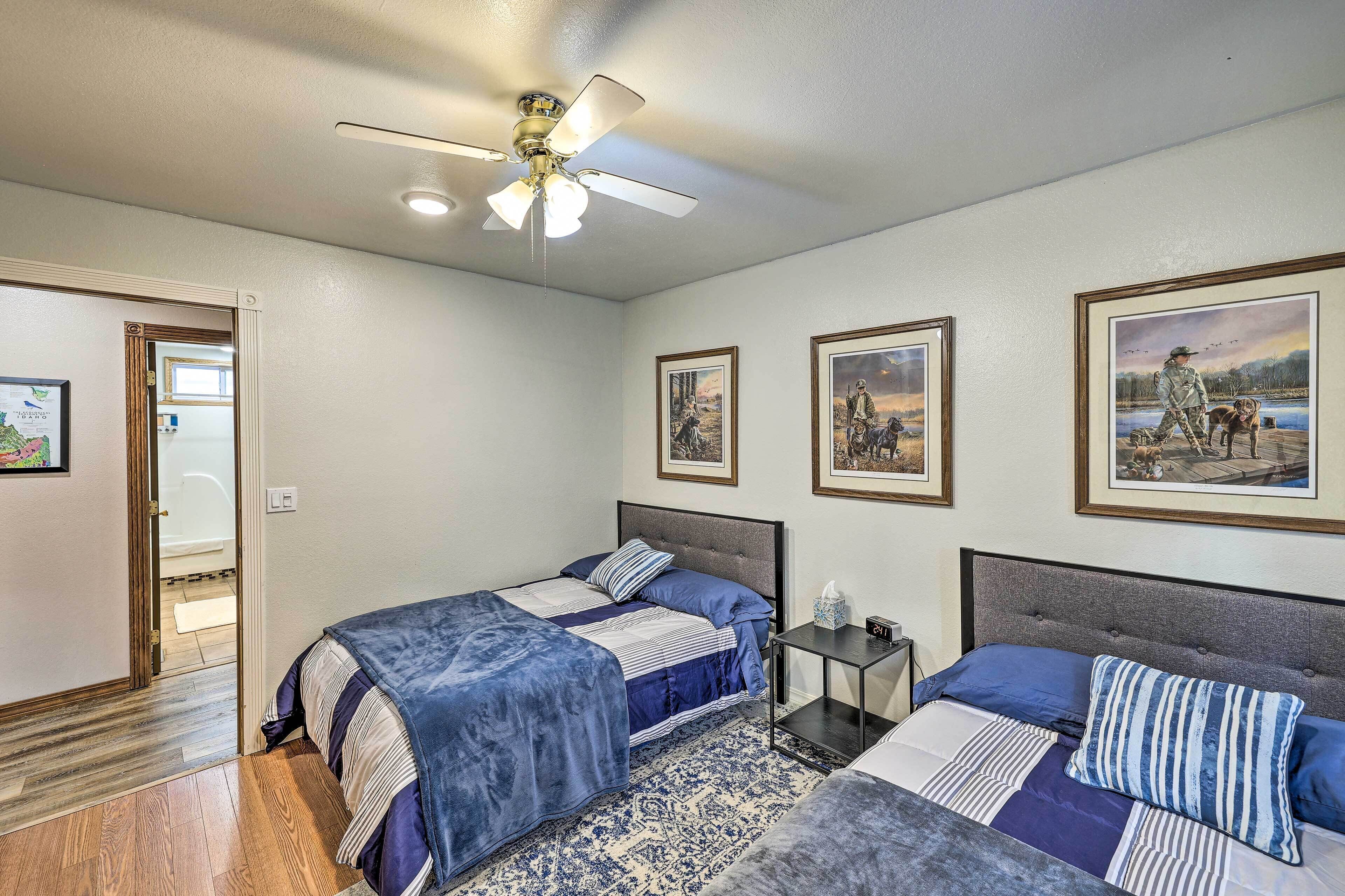 A bedroom with two beds, a ceiling fan, framed pictures on the wall, and a wooden floor.