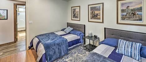 A bedroom with two beds, a ceiling fan, framed pictures on the wall, and a wooden floor.