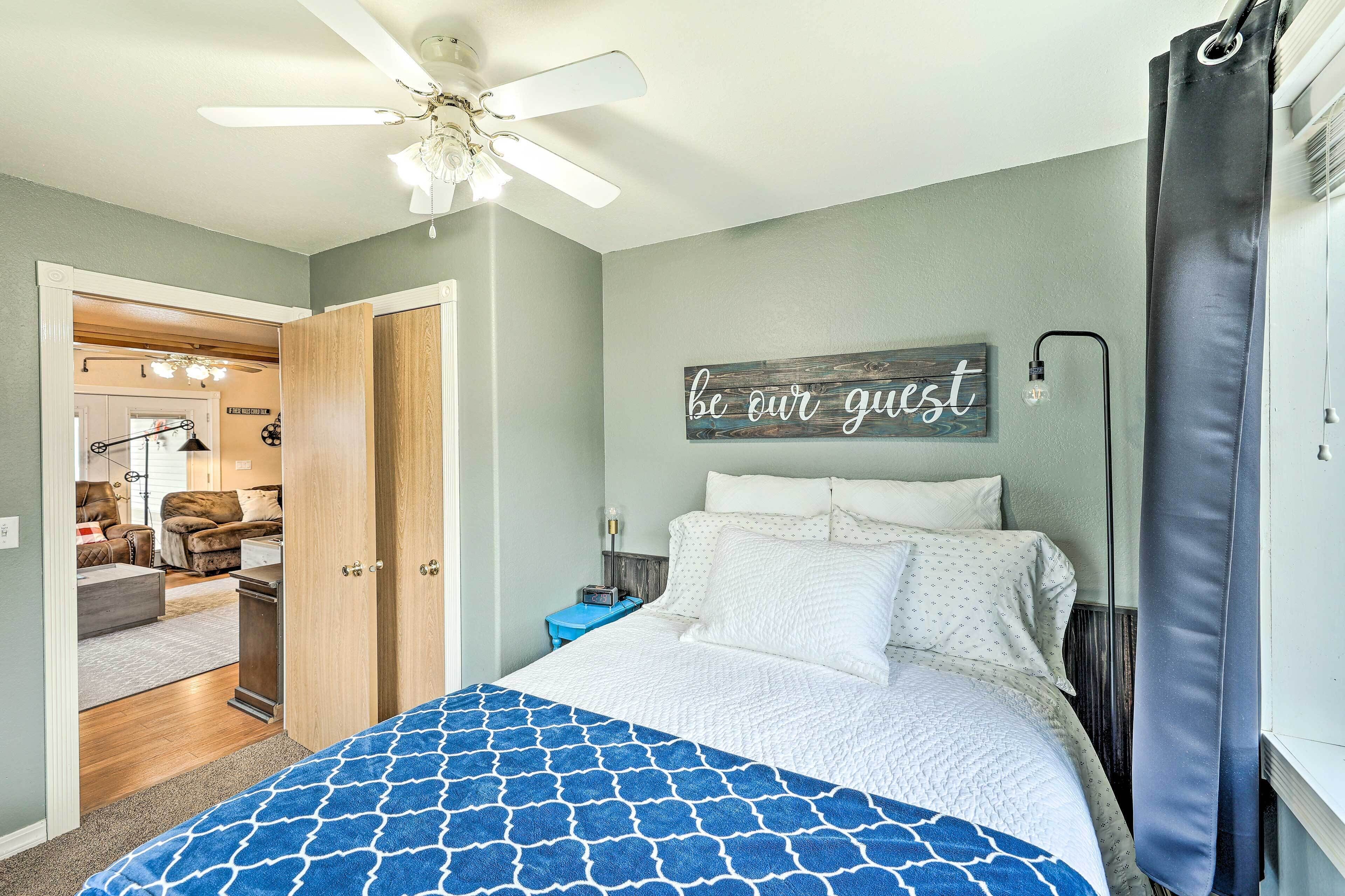 A bedroom with a bed, a ceiling fan, a wall sign, and a door leading to another room.