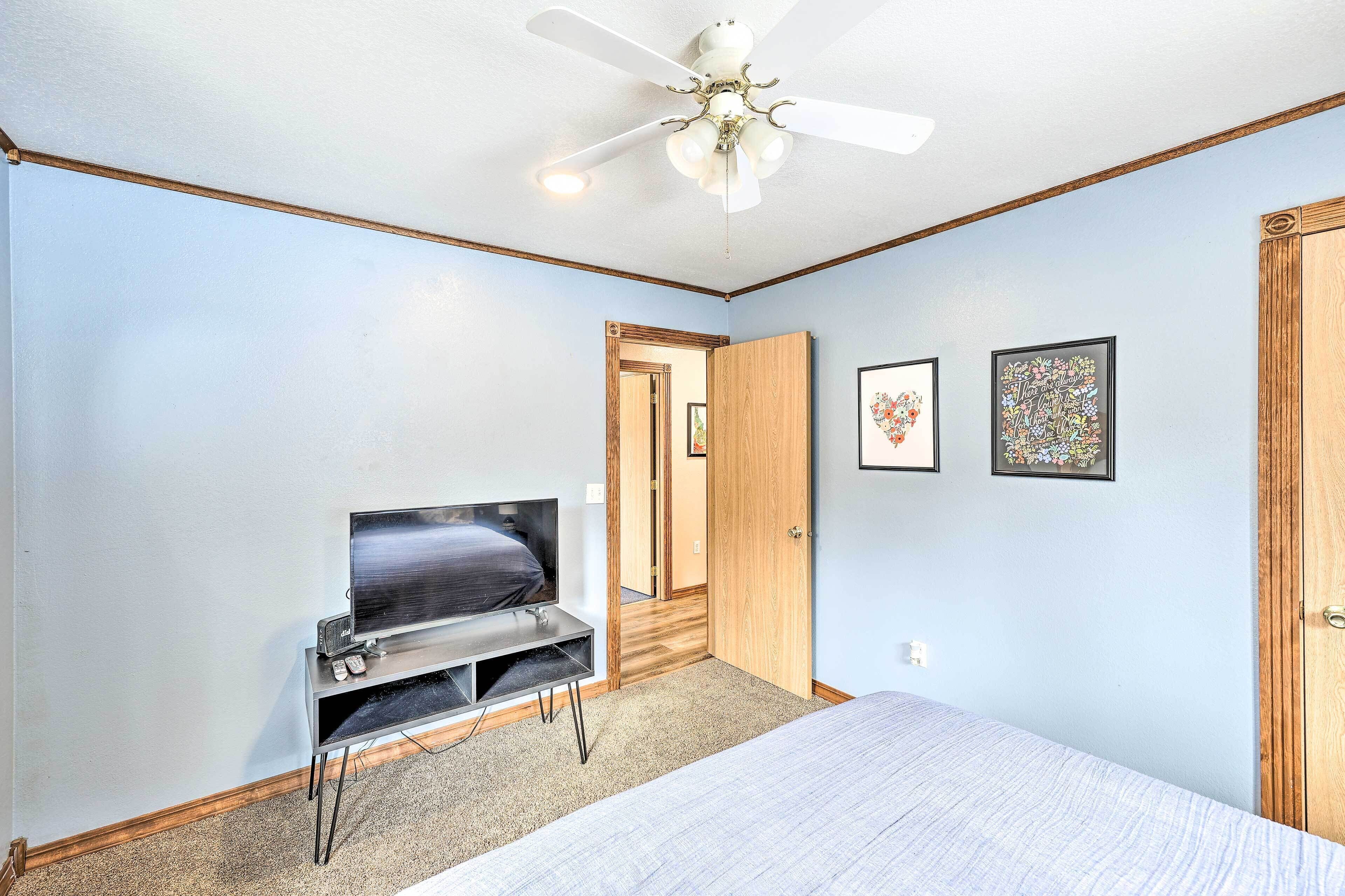 Une chambre à coucher avec un lit, un téléviseur posé sur un meuble, un ventilateur de plafond et deux tableaux encadrés accrochés au mur.