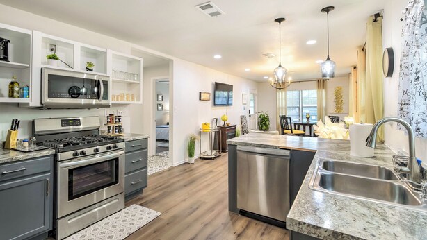 A modern kitchen with stainless steel appliances, a central island with a sink, and a dining area in the background. - Lovely Historic Fort Worth Home w/ Deck (Fort Worth)