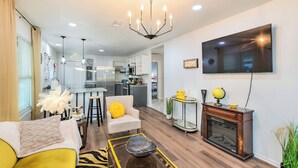 A modern living room with a sofa, a coffee table, a TV mounted on the wall, and a fireplace. - Lovely Historic Fort Worth Home w/ Deck (Fort Worth)