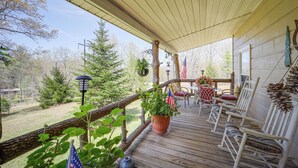 Une terrasse en bois avec des sièges d’extérieur, un pot de fleurs orné d’un drapeau américain et une vue sur les arbres environnants.