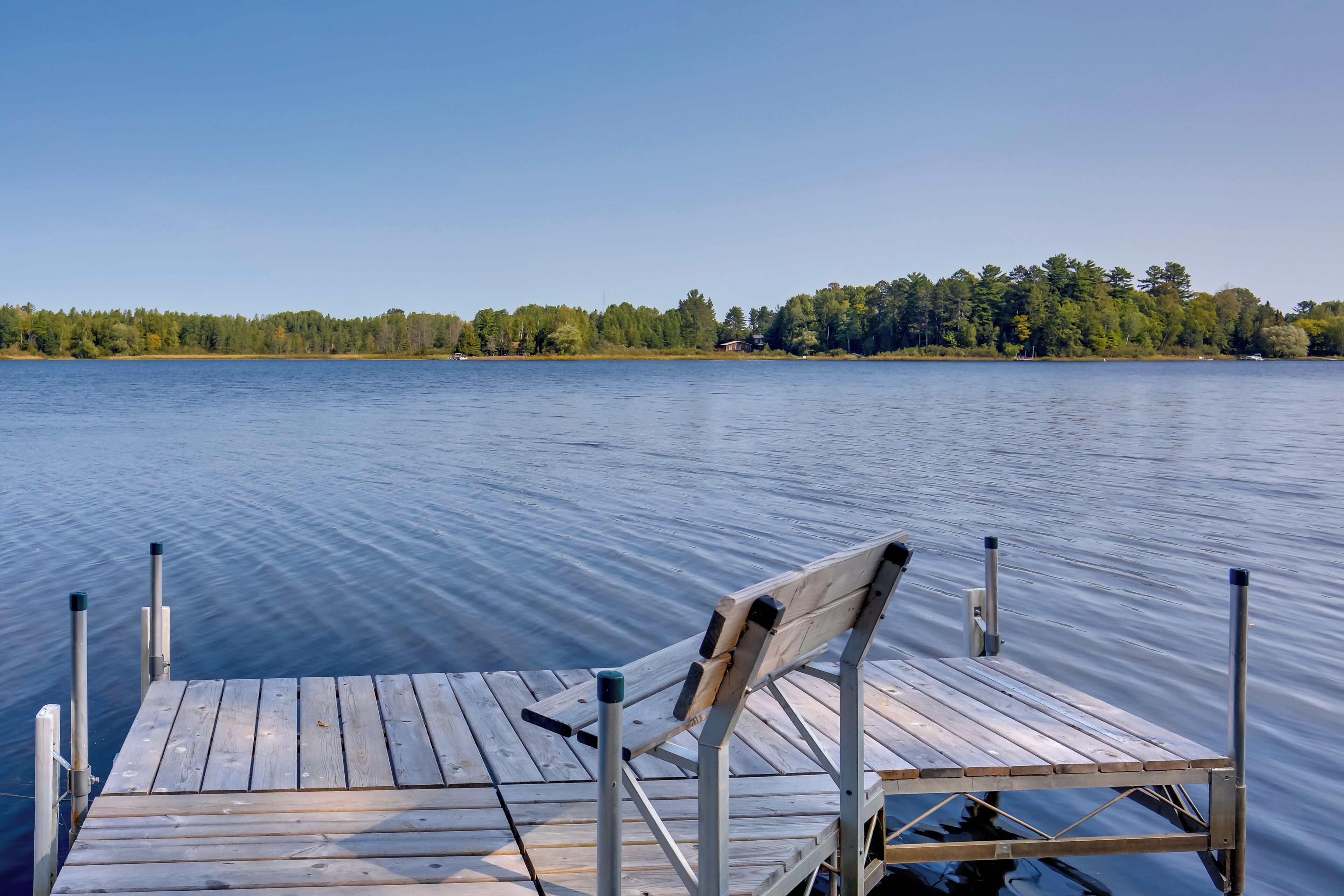 A wooden dock extending into a calm lake with a chair on it.