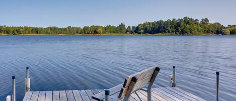 A wooden dock extending into a calm lake with a chair on it.