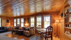 Un interior de cabaña acogedor con paredes de madera, una mesa de comedor con sillas, un sofá y una chimenea.