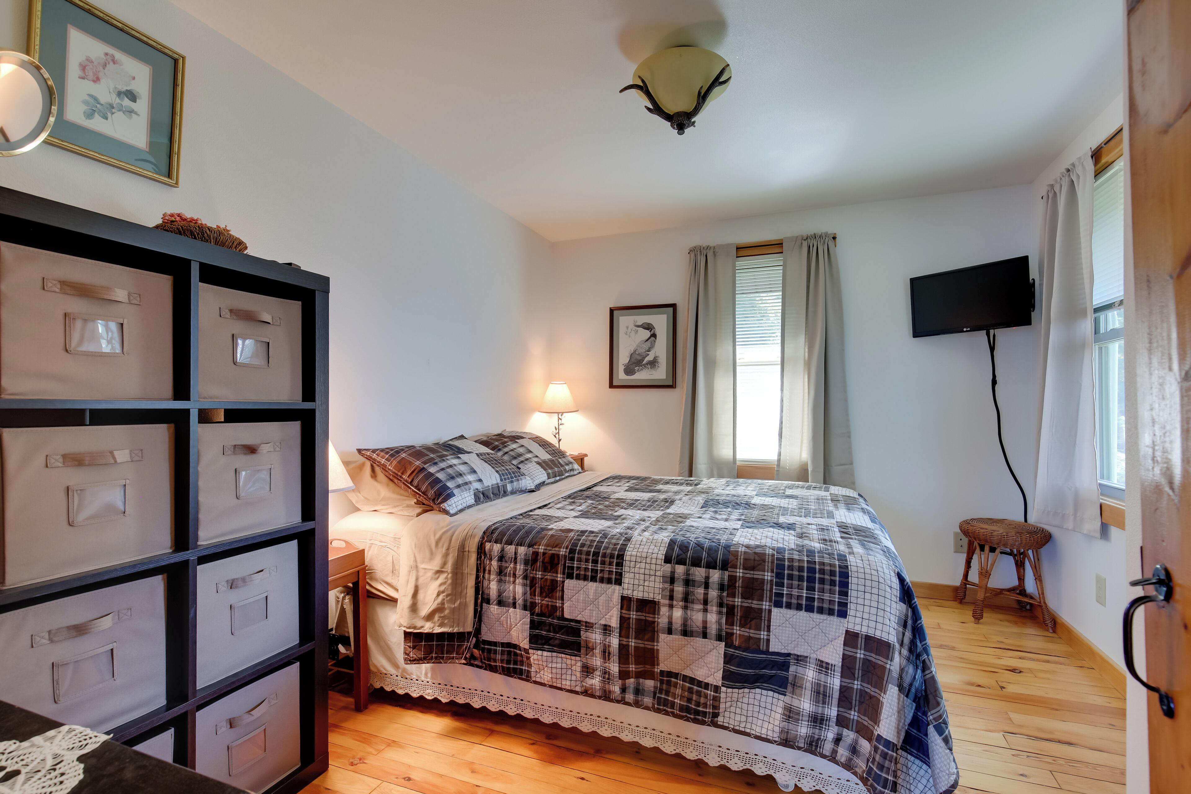 A bedroom with a bed, a nightstand, a lamp, a television, a wall-mounted shelf, and a window with curtains.