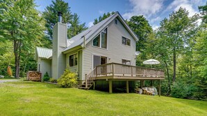 Une maison à deux étages dotée d’une terrasse, entourée d’une végétation luxuriante.