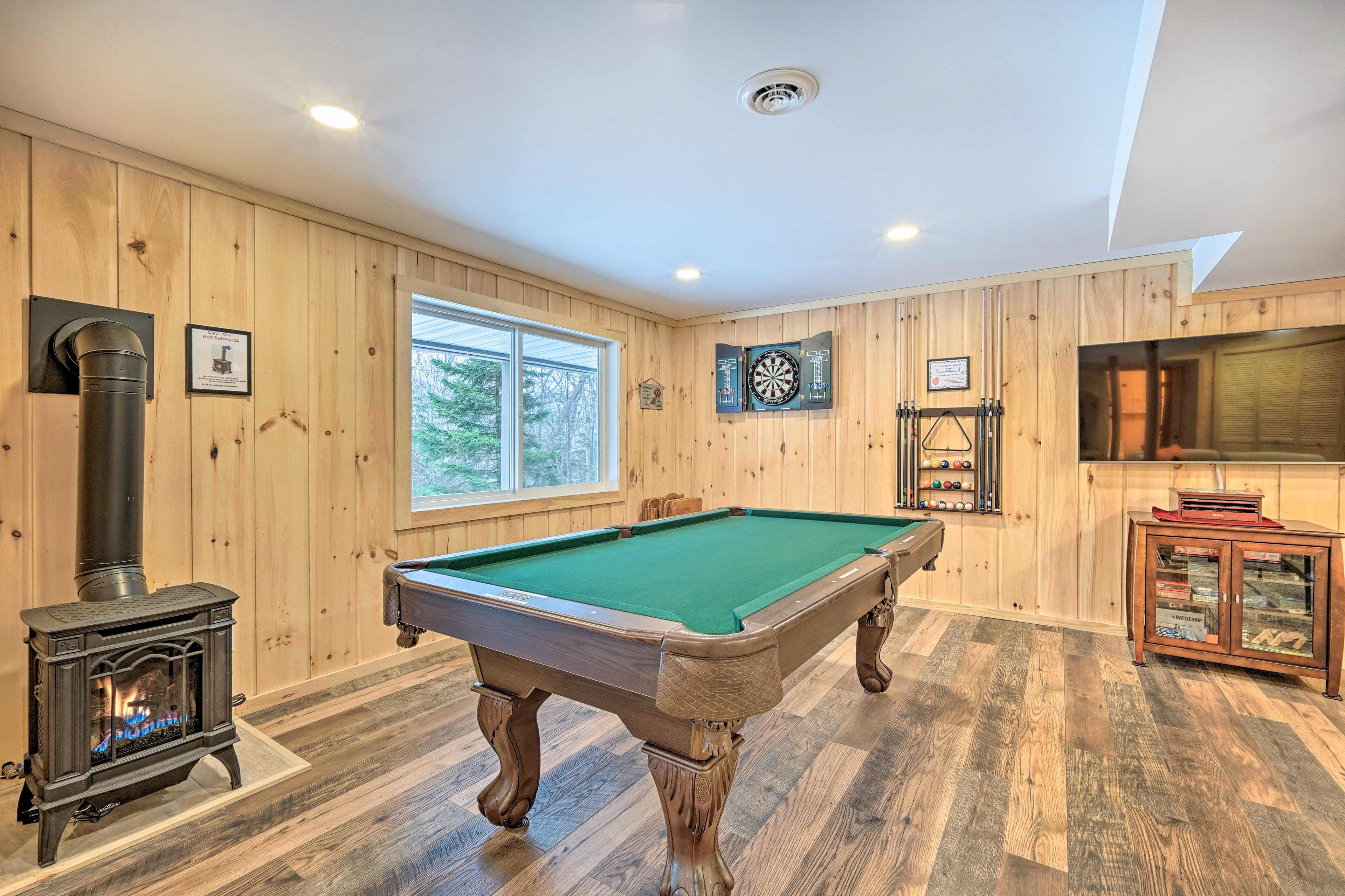 A pool table in a room with wooden walls, a large window, and a fireplace.