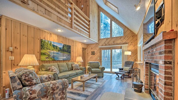 Un salon spacieux aux murs en bois et doté d’une cheminée, comprenant un canapé, des fauteuils et une grande fenêtre.
