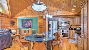 A cozy cabin interior with a wooden ceiling, a dining area with a round table and chairs, a kitchen with modern appliances, and a living room with a sofa and a TV.