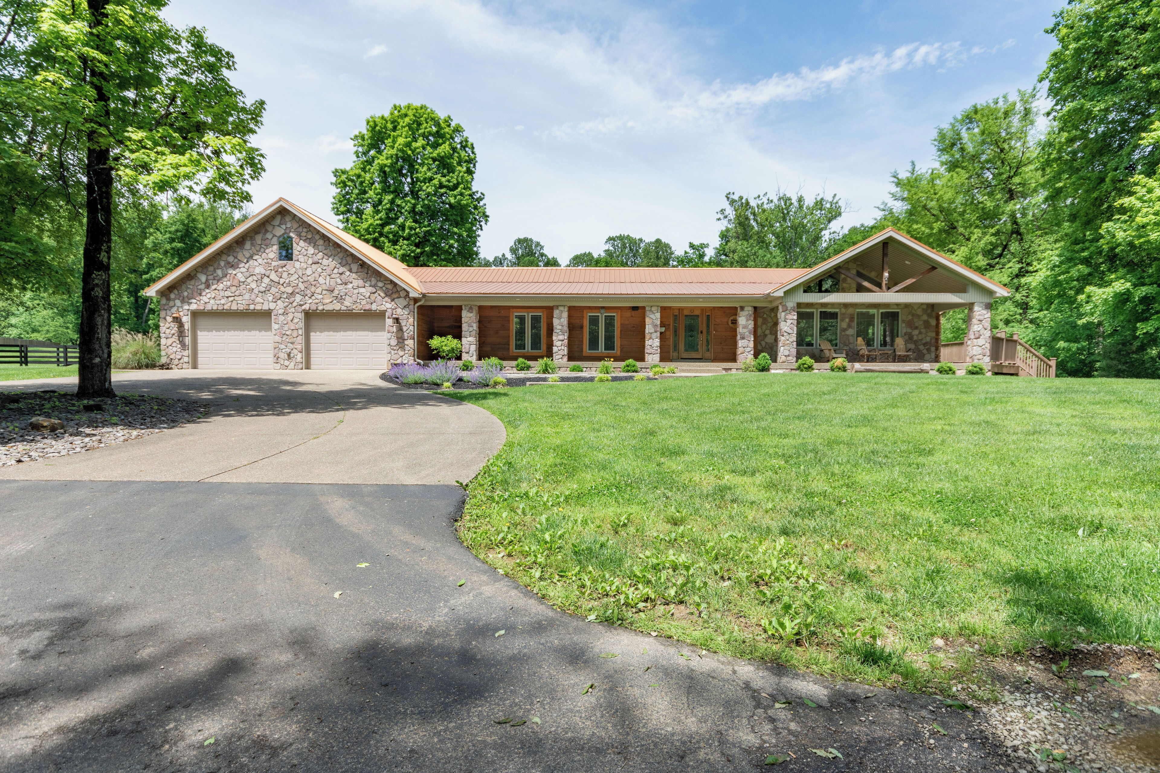 A two-story stone house with a large garage, a covered porch, and a well-maintained lawn.