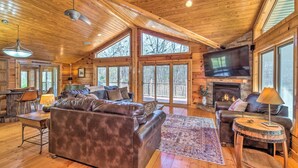 A cozy cabin interior with a large leather sofa, a fireplace, and a television mounted on the wall.