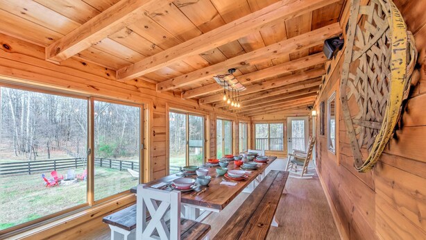 A wooden cabin with a long dining table set for a meal, large windows, and a view of the outdoors.