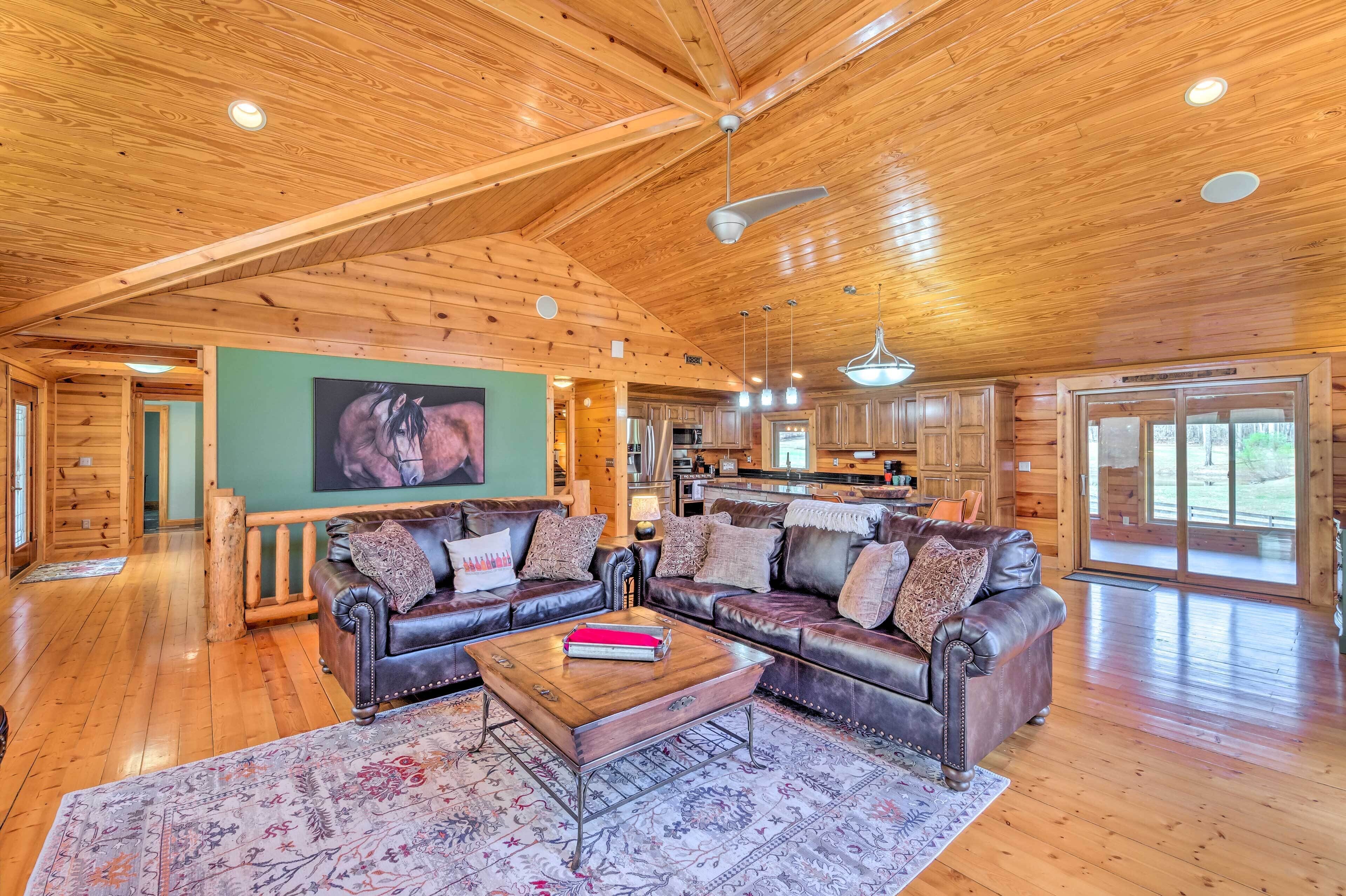 A spacious living room with wooden floors and high ceilings, featuring leather sofas, a coffee table, and a large painting on the wall.