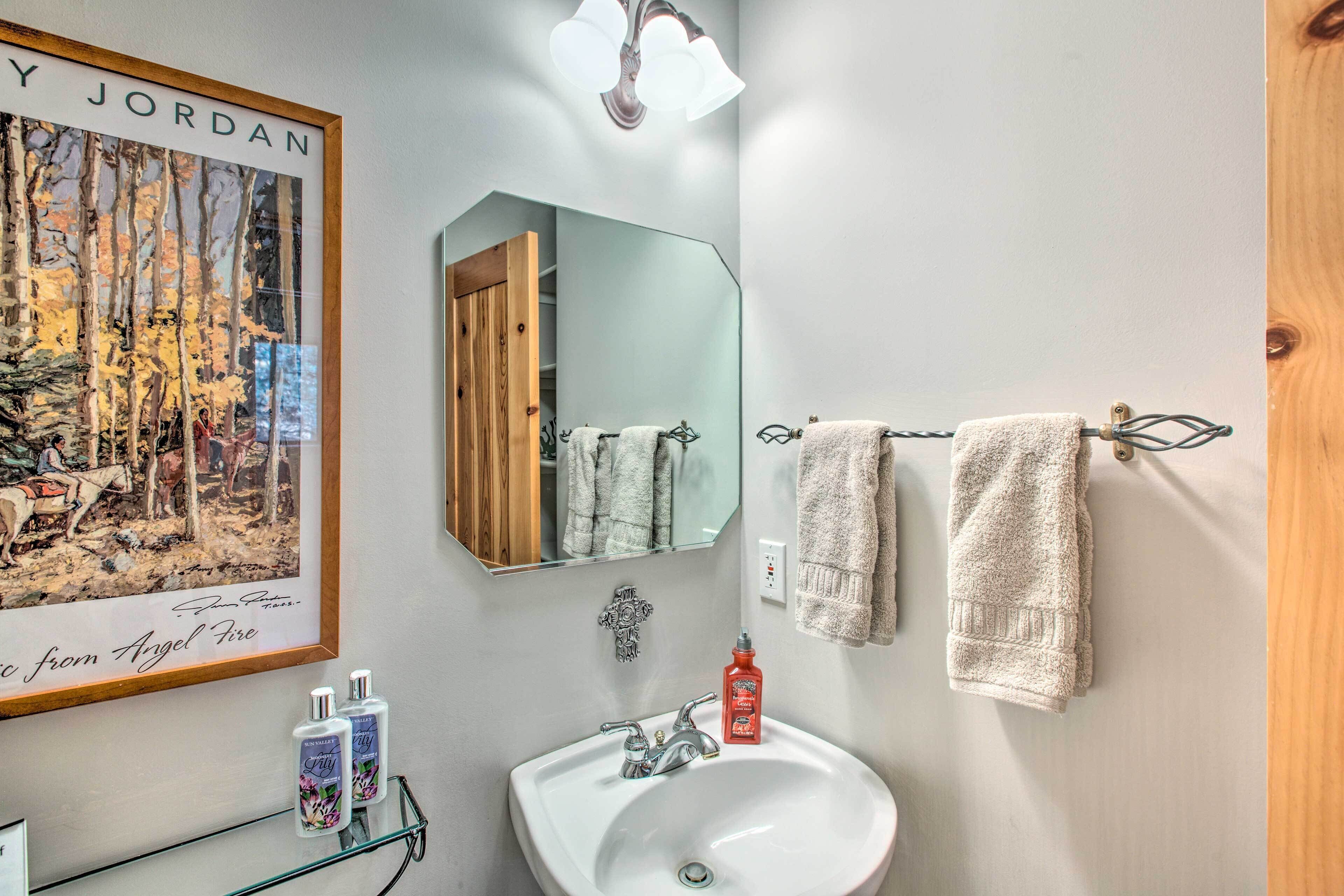 Une salle de bain avec un lavabo blanc, deux serviettes, un tableau encadré et un miroir.