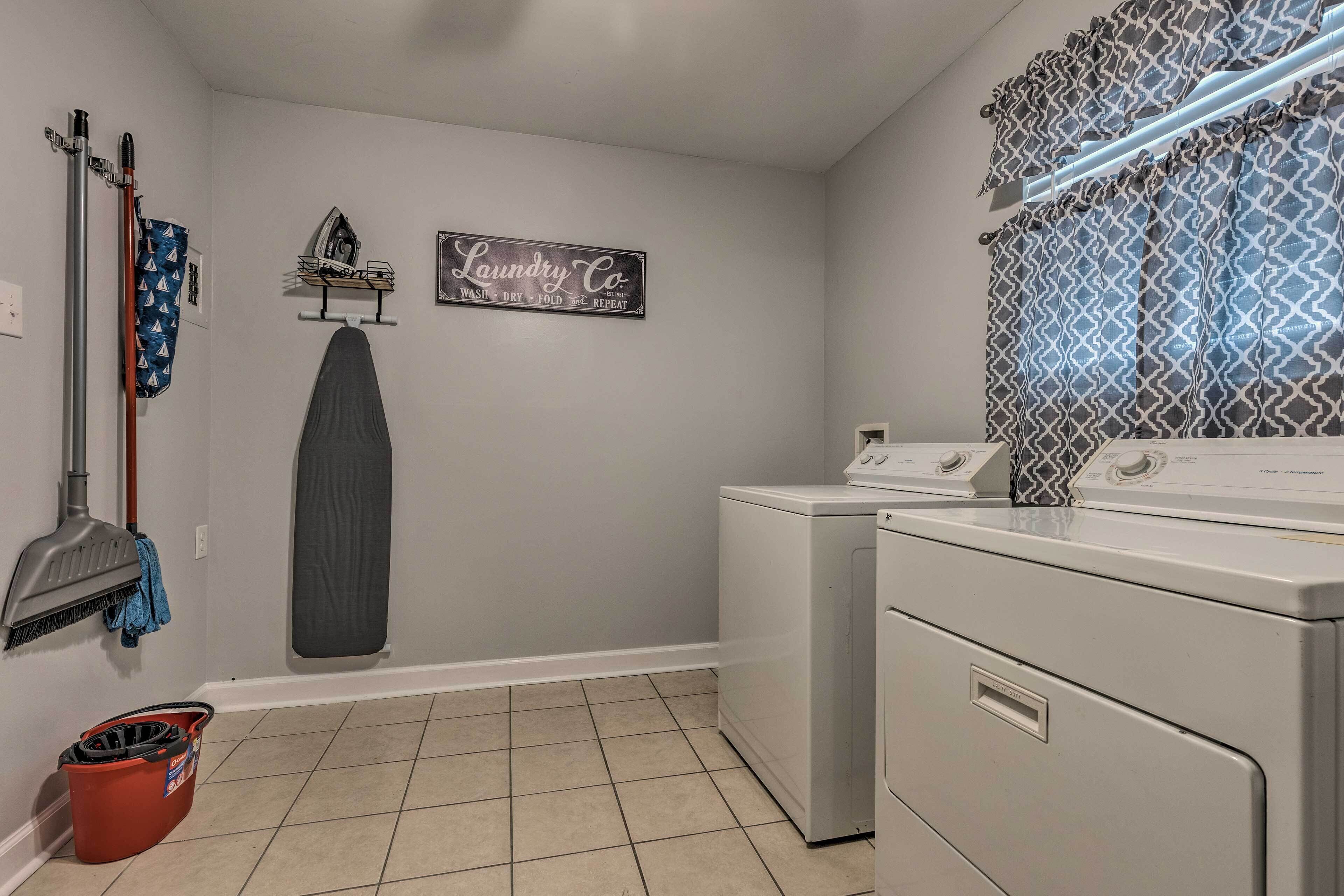 A laundry room with a washing machine, a dryer, a mop, a bucket, and a wall-mounted ironing board.