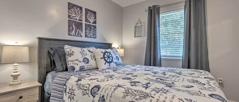 Un dormitorio con cama, mesitas de noche, lámpara de noche, ventilador de techo, ventana con cortinas y decoración en la pared.
