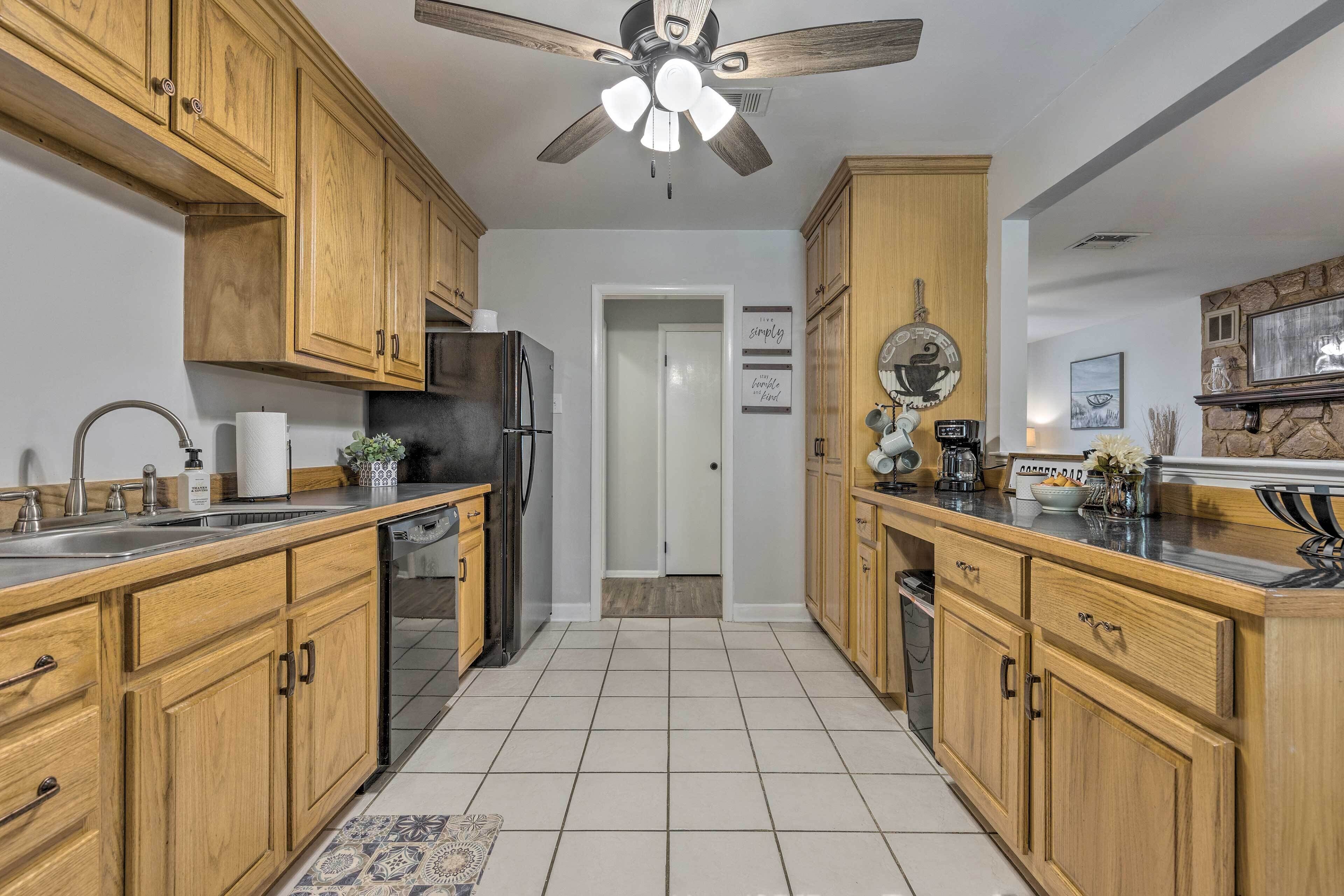 A kitchen with wooden cabinets, a stainless steel refrigerator, a ceiling fan, and a tiled floor.