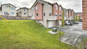 A residential area with multiple two-story houses, a grassy slope, and a driveway with parked cars. - Sleek Escape w/ Balcony < 1 Mi to 5th Avenue! (Anchorage)