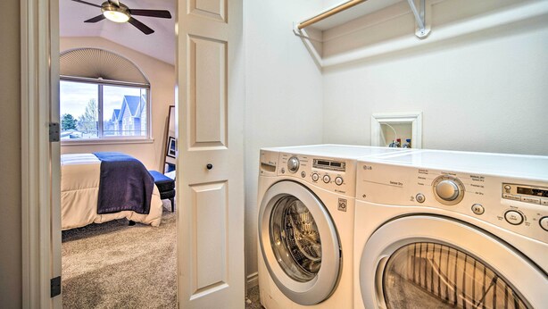 A laundry room with a front-loading washer and dryer, a ceiling fan, a window, and a door leading to a bedroom. - Sleek Escape w/ Balcony < 1 Mi to 5th Avenue! (Anchorage)