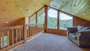 A cozy cabin with a wooden interior, a balcony with a railing, and a large window offering a view of the forest. - Cabin Near Grand Lake' w/ Private Deck! (Fairland)