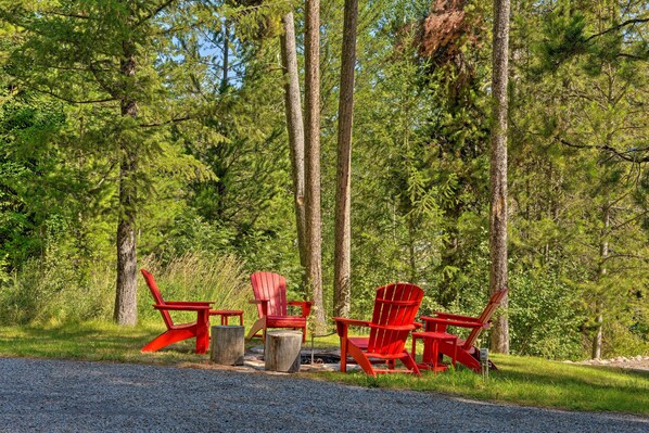 A forest setting with red Adirondack chairs and a fire pit.