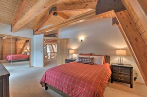 Un dormitorio con techo inclinado, una cama con colcha escocesa roja, una mesita de noche con lámpara y un armario de madera.