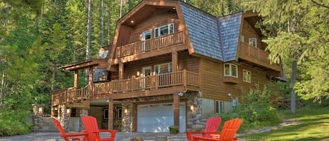 A multi-level log cabin with a stone foundation, a balcony, and a garage.