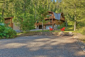 A two-story log cabin with a stone foundation, a balcony, and a gravel driveway.