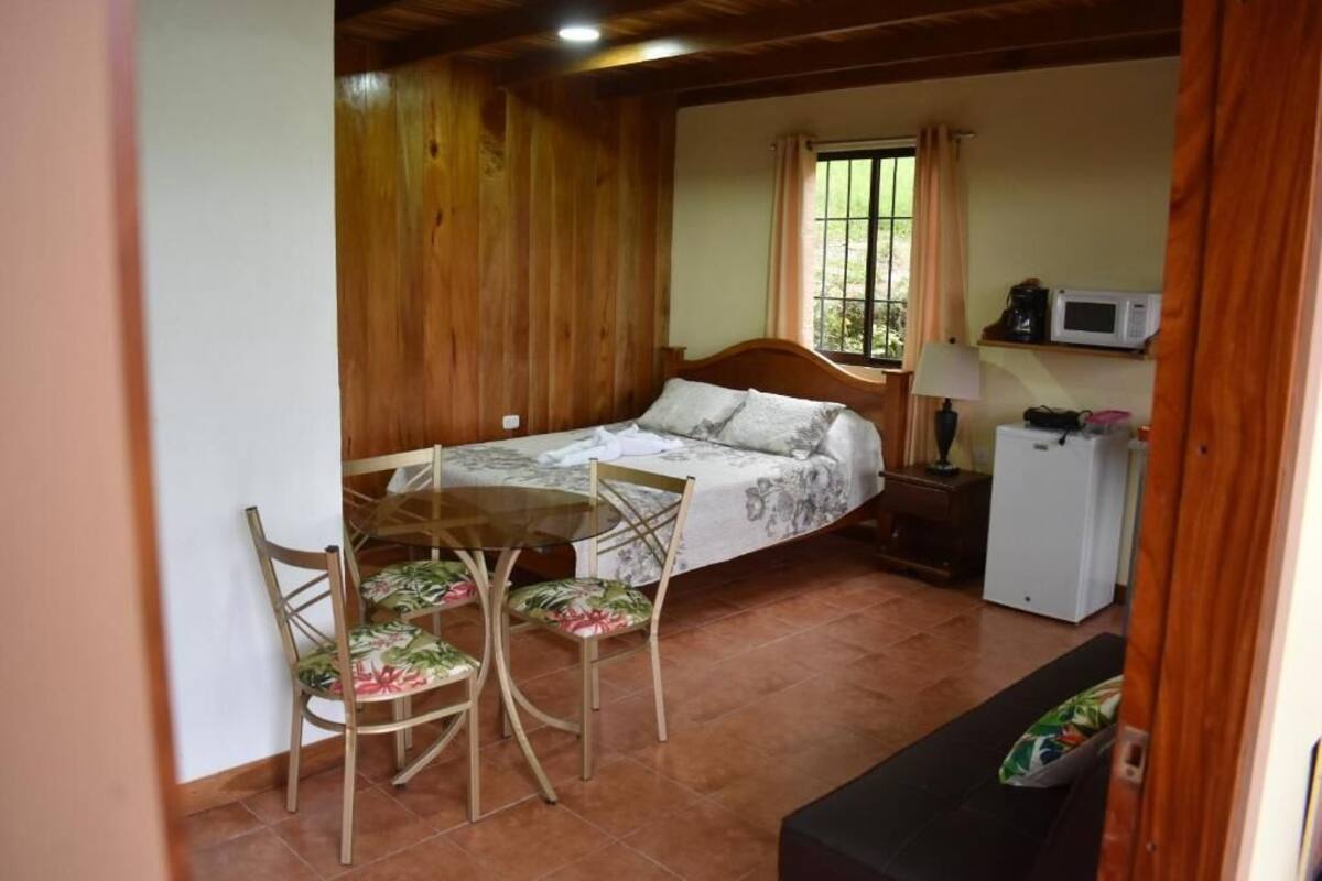 A cozy room with a bed, a small table with chairs, a microwave, and a window with curtains.