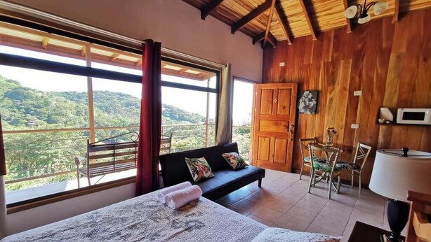A bedroom with a large bed, a sofa, a dining table, and a view of the outdoors. - Apartments Monte Luna Mountain View (Monteverde)