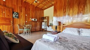 A wooden-finished room with a bed, a sofa, a desk, and a chair. - Apartments Monte Luna Mountain View (Monteverde)
