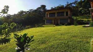 A two-story building with a flat roof and large windows, surrounded by a well-maintained lawn and trees. - Apartments Monte Luna Mountain View (Monteverde)