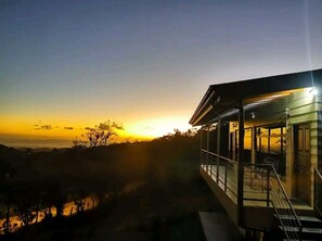 A modern building with a balcony overlooking a sunset.