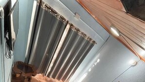 Une pièce avec un escalier, une petite table recouverte d’une nappe à carreaux, un fauteuil rembourré et une fenêtre avec des rideaux.