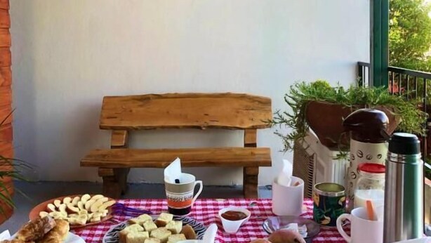 Un espace extérieur accueillant avec un banc en bois, une table dressée avec des pâtisseries, des tasses à café et une pancarte indiquant « hosteria ma ma du ».