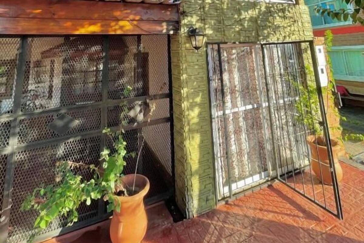 Una casa con entrada protegida por un portón, un pequeño porche y una planta en maceta.