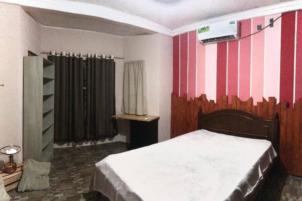 Un dormitorio con cama, mesita de noche, lámpara, radiador y cortinas.