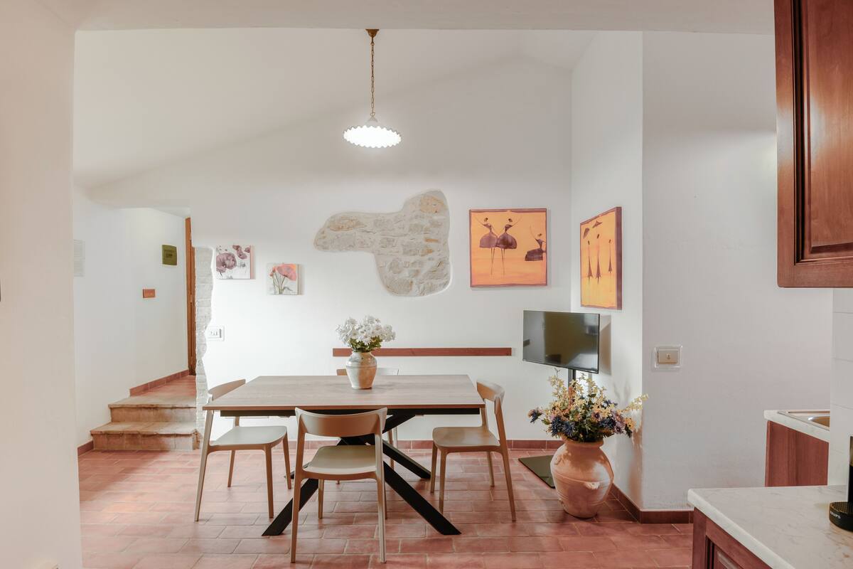 Uma área de refeições com mesa e cadeiras de madeira, um vaso com flores e obras de arte nas paredes.