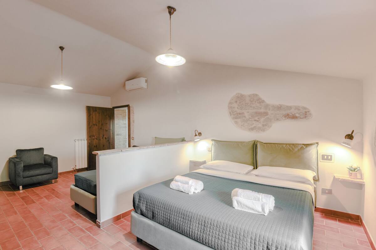 Quarto com cama, poltrona, mesa de cabeceira e luminária na parede.