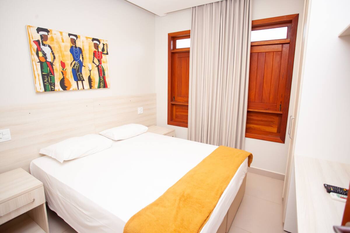 Una camera d'hotel con un letto, un comodino, una porta in legno e un quadro appeso al muro.