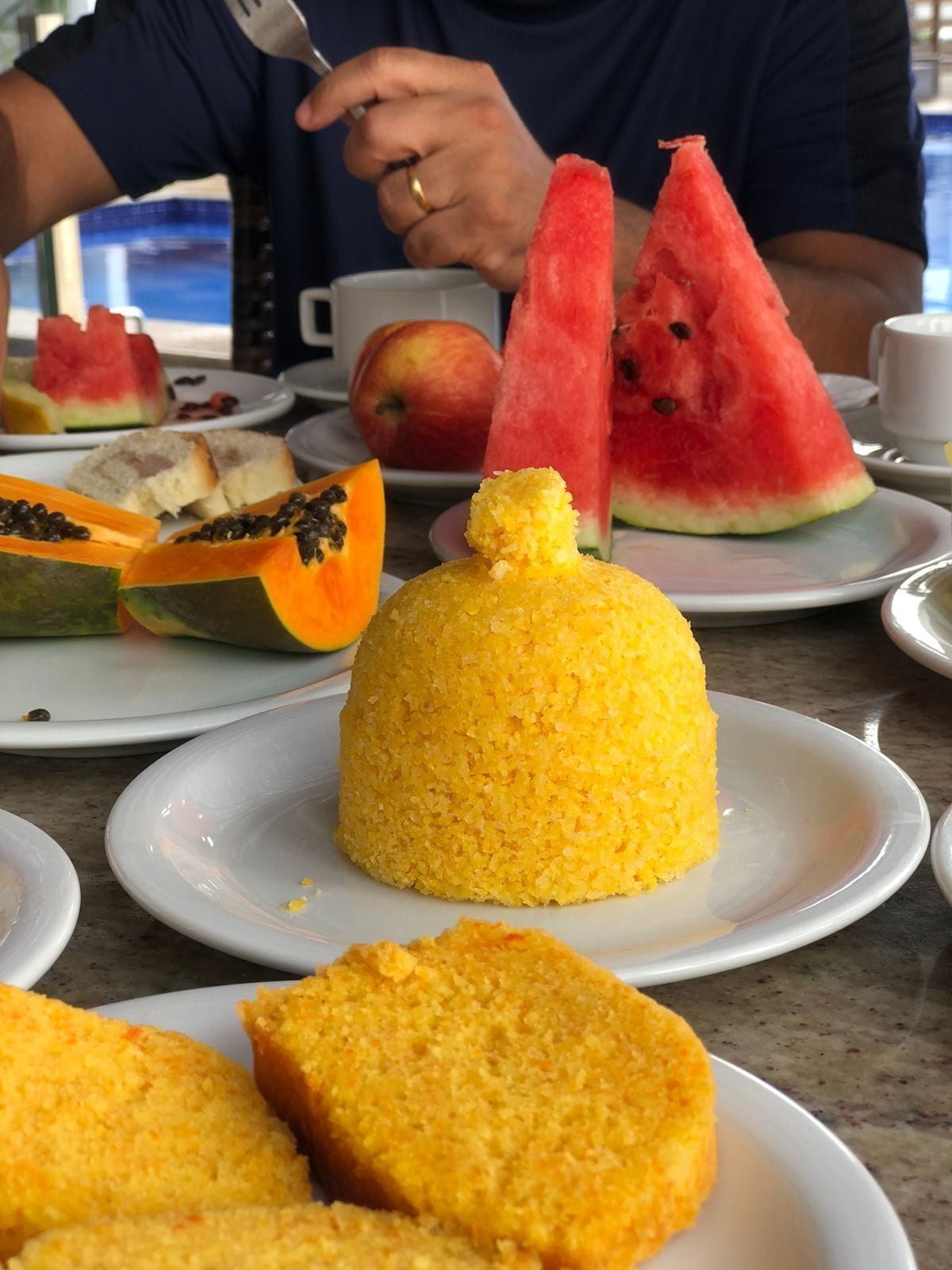 A table with various food items including a yellow cornbread, watermelon slices, and a papaya.