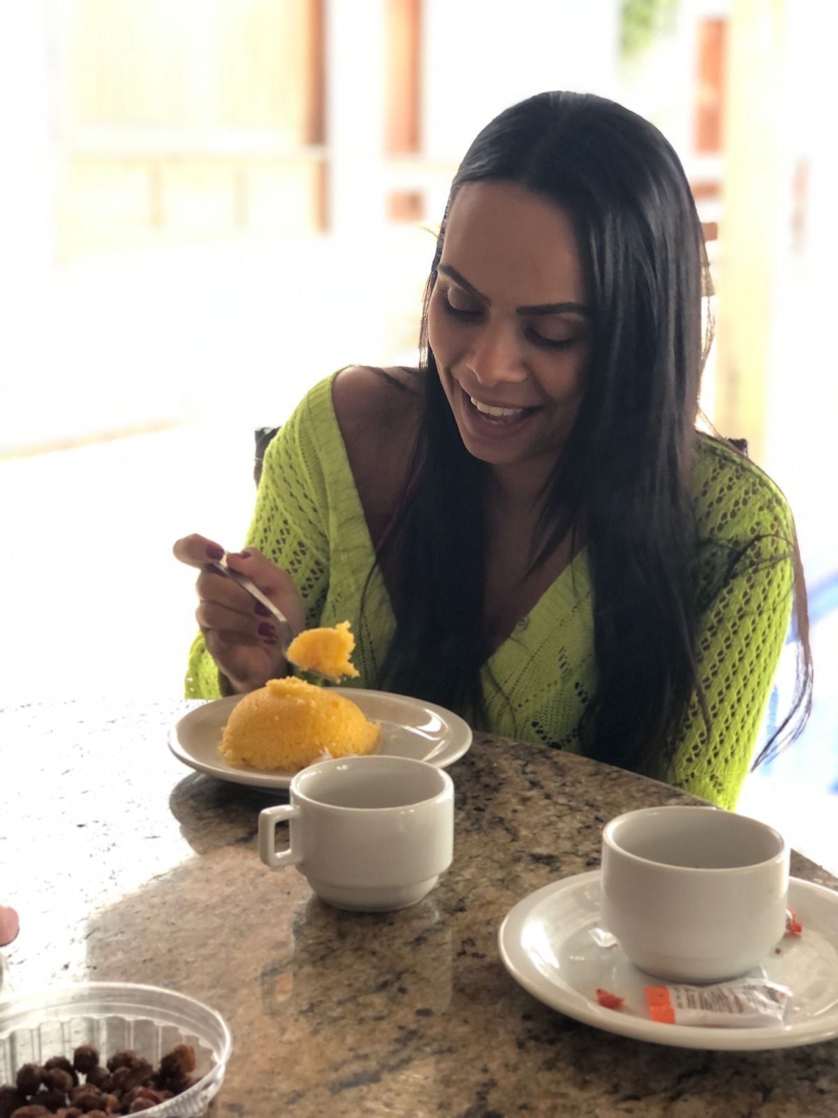 A person sitting at a table with a plate of food, two white cups, and a bowl of nuts.