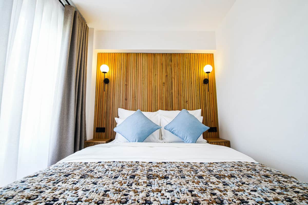 Habitación de hotel con una cama, dos almohadas, un tapete estampado y paneles de madera en la pared.