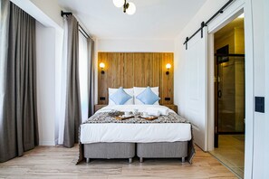 A hotel room with a large bed, two bedside tables, a wooden headboard, and a glass shower area. - Sisu Bozcaada (Bozcaada)