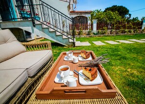 A wicker sofa and a wooden tray with a slice of cake, a cup of coffee, and a teapot on a grassy lawn. - Sisu Bozcaada (Bozcaada)