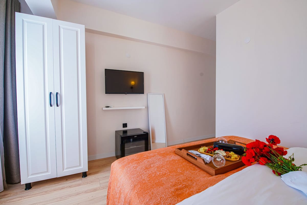 Una habitación de hotel con una cama, un televisor, un armario y una bandeja con flores y aperitivos.