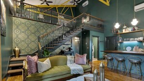 Un salon chaleureux avec un canapé vert, un pouf blanc et un escalier menant à un niveau supérieur.