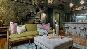Un salon chaleureux avec un canapé vert, un pouf blanc et un escalier menant à un niveau supérieur.